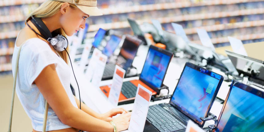 Jeune femme regardant un modèle récent d’ordinateur portable dans un magasin d’électronique