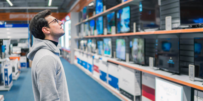 Smart modern male customer choosing large TV-sets at electronics store. He looks wondered. New screen generations.