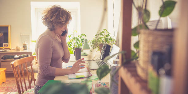 Femme travaillant à domicile, téléphonant et s’apprêtant à écrire dans un agenda.