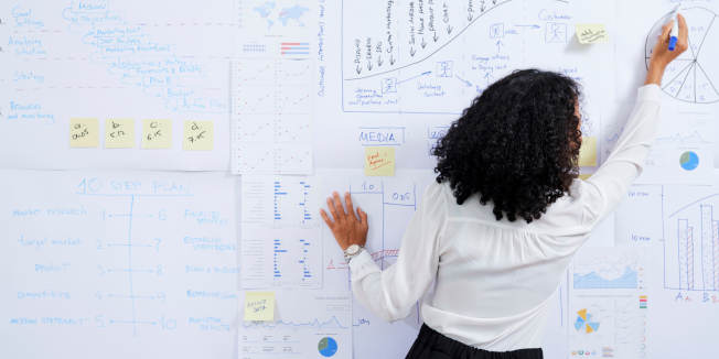 Vue arrière d'une femme d'affaires avec un diagramme de dessin de cheveux bouclés sur le tableau blanc lors de la préparation de la présentation