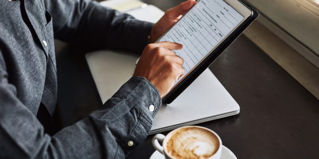 Schnappschuss eines nicht erkennbaren Mannes, der ein digitales Tablet nutzt, während er in einem Café sitzt