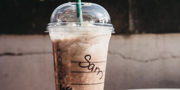 Starbucks-Eiskaffee mit Sahne im durchsichtigen Plastikbecher mit dem Namen Sam auf einem Tisch im Sommer.