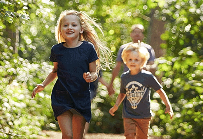 Zwei Kinder laufen durch einen hellen, sonnigen Wald.