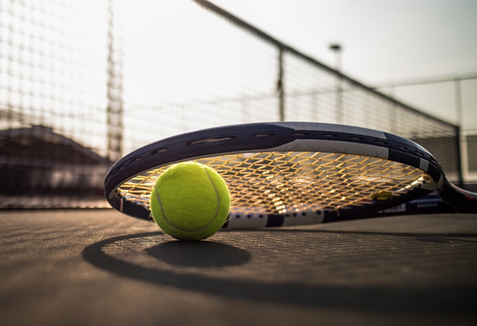 Raqueta de tenis apoyada sobre una pelota de tenis