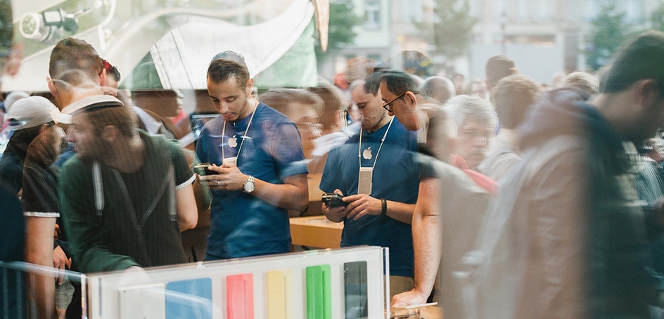 Two Apple employees seen through the reflection of a window on a busy street