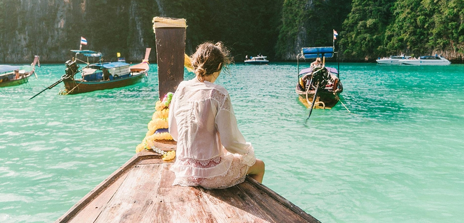 Mujer sentada en la cubierta de un pequeño barco de madera en aguas tropicales