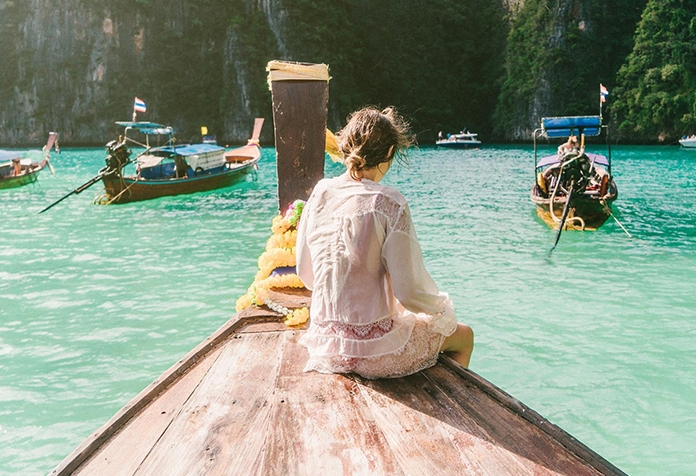 Frau sitzt auf dem Deck eines kleinen Holzbootes in tropischen Gewässern