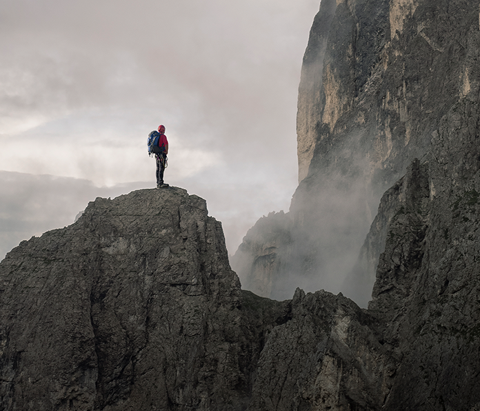 Fernaufnahme eines Bergsteigers, der bei nebligem Wetter auf einem Felskamm steht.