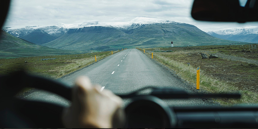 View of a road leading to mountains from the driver's seat of a car