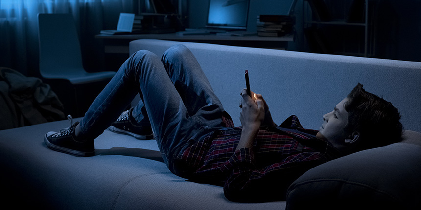 Junger Mann auf dem Sofa schaut auf sein Smartphone