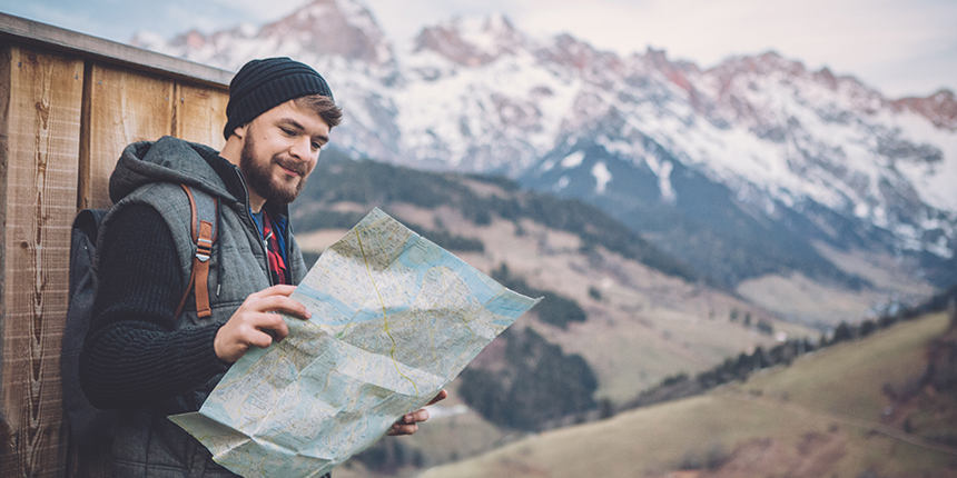 Young hiker examining a fold-out map with mountains in the background