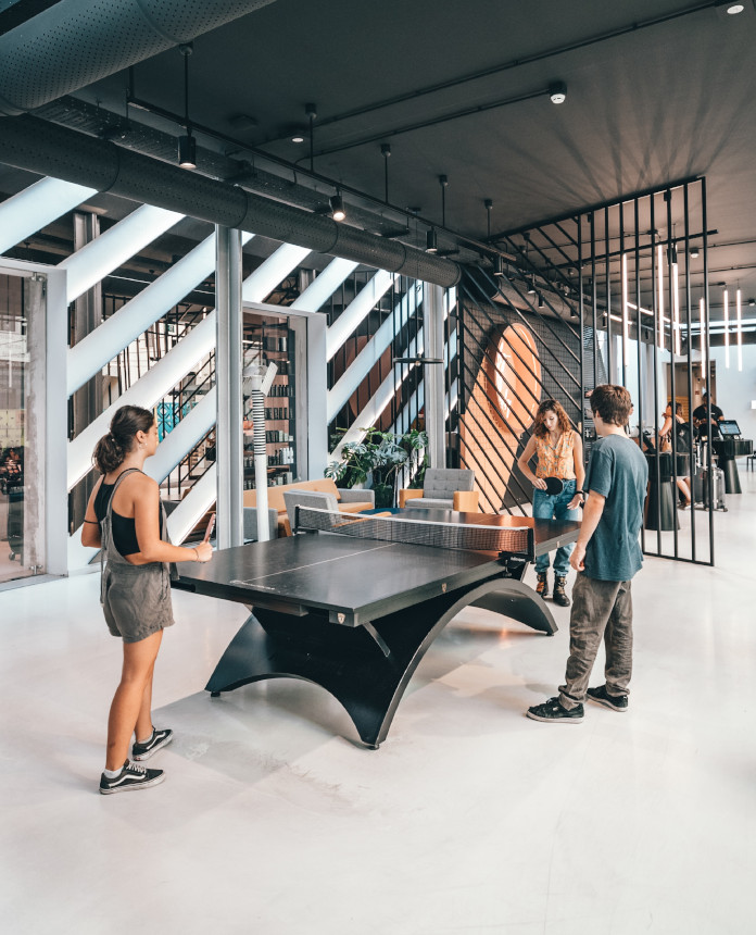 Two women playing ping pong while a man is watching the match