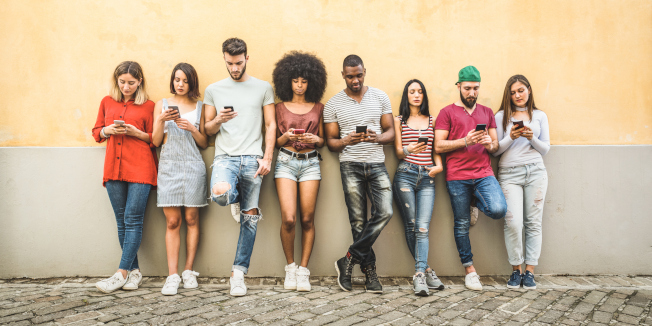 Freunde aus allen Teilen der Welt, die gegen die Wand im Hinterhof des Universitätskollegs ihre Smartphones benutzen - Junge Leute, die süchtig nach Smartphones sind - Technologiekonzept mit immer verbundenen Millennials