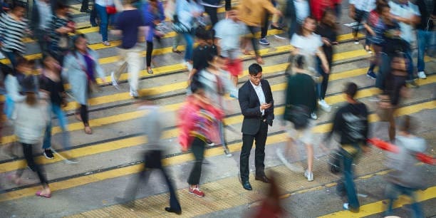 Vue en hauteur d'un homme d'affaires utilisant un smartphone au milieu de la foule. Le professionnel se tient dans une rue très fréquentée. Il est entouré par les gens de la ville