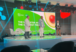 Three people standing on a stage with a bright green presentation screen in the background.