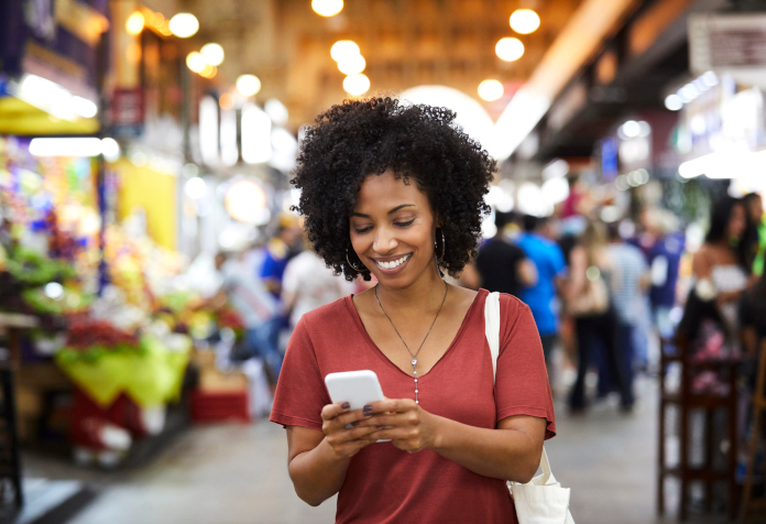 Woman smiling and looking at her smartphone in a bustling indoor market.