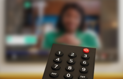 Remote control pointed at a blurred television screen.