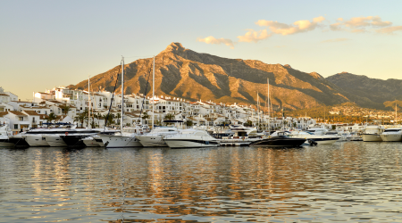 Puerto con barcos y montañas al fondo iluminado por la luz del atardecer.