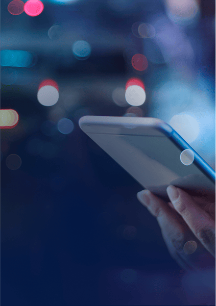Hand holding a smartphone with a blurred cityscape background and bokeh lights.