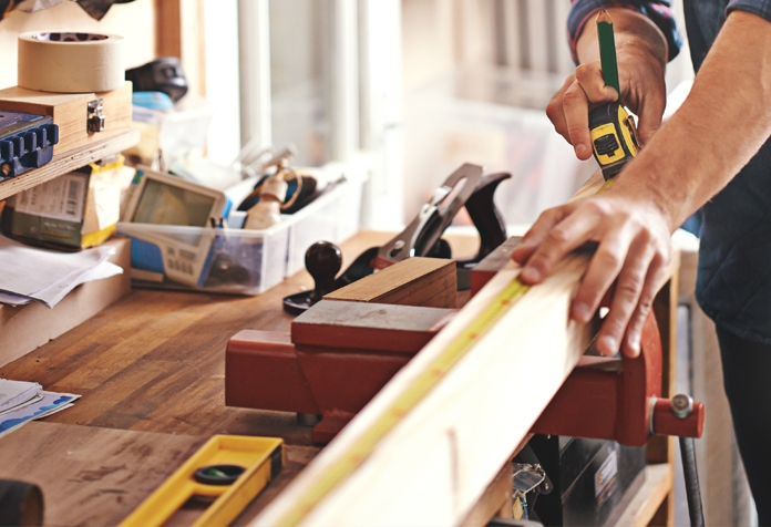 Homme mesurant un morceau de bois fixé à un établi