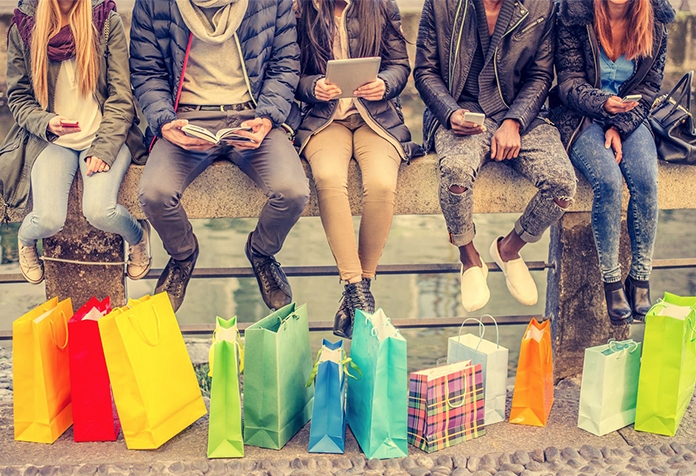 Bolsas de compras colocadas debajo de una fila de personas sentadas en una gran banca de concreto