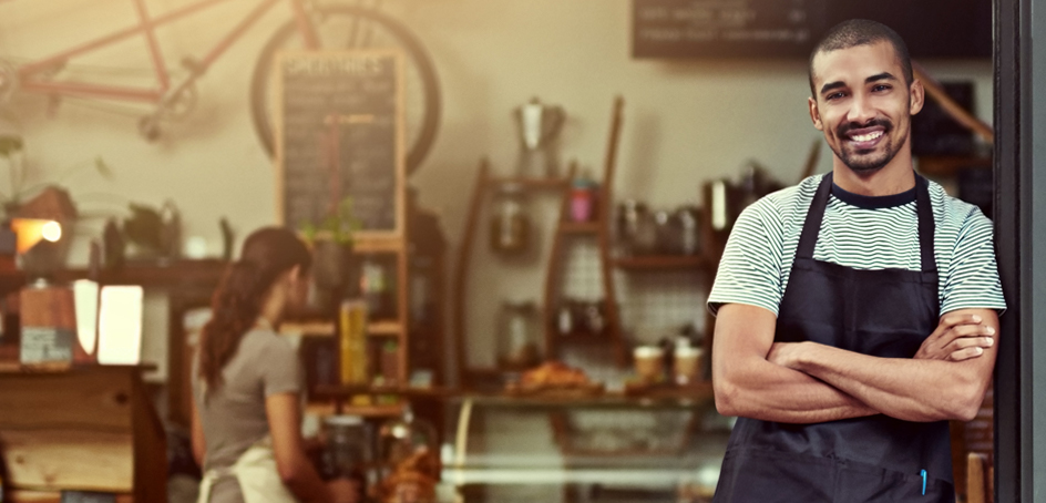 Coffee shop worker smiling at his shop door.