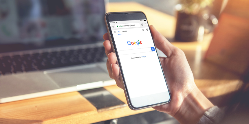 Hand holding a cell phone showing Google search engine page.