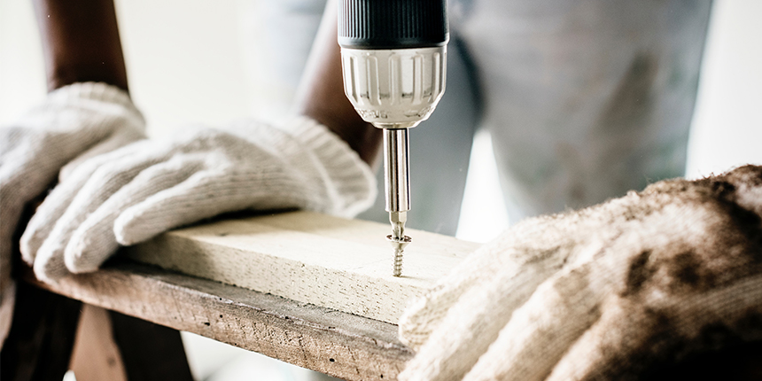 Hands drilling a screw into a piece of wood.