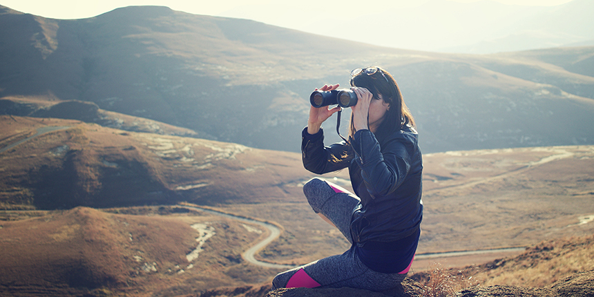 Femme assise au sommet d’une montagne regardant dans des jumelles
