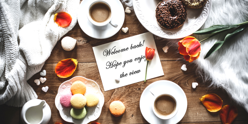 Top view of table with blank greeting card, macaroons, donuts, coffee and decorations.