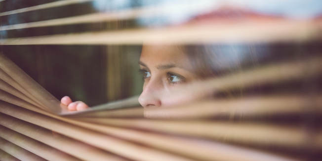 Woman at home looking through the blinds.