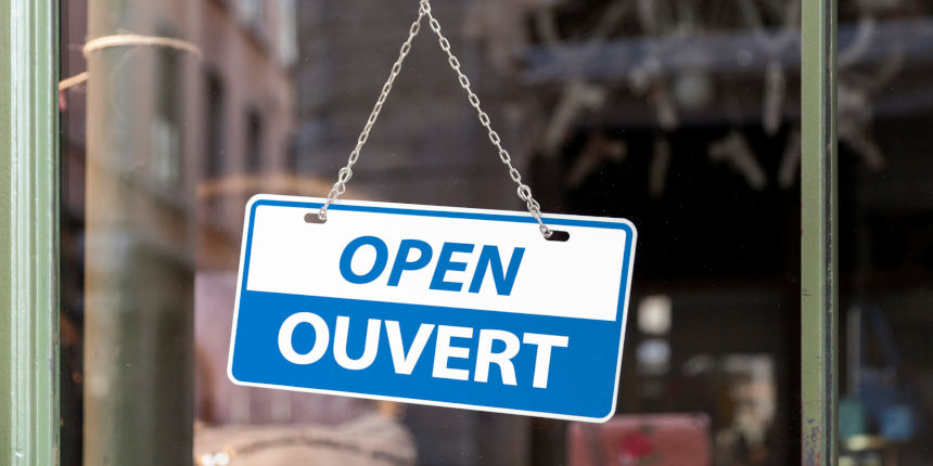 Close-up on a blue Open sign in a window with written in it in English & French.