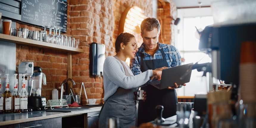 Two colleagues in a coffee shop looking at a laptop